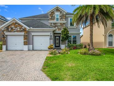 Charming two-story home featuring a stone facade, lush landscaping, and a three-car garage at 2669 Sand Hill Point Cir, Davenport, FL 33837
