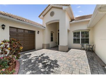 Charming, light-colored home featuring a well-manicured front yard, brown garage door and a cozy table and chairs on the side at 3856 Shoreside Dr, Kissimmee, FL 34746