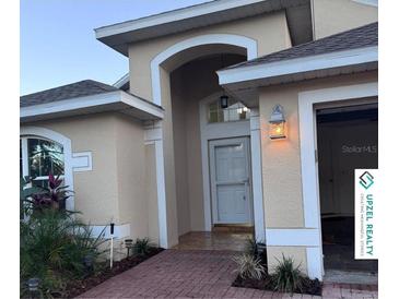 Inviting home featuring a welcoming front entrance with an arched entryway, brick path, and manicured landscaping at 117 Winchester Ln, Haines City, FL 33844