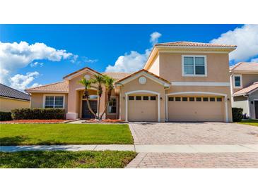 Charming two-story home featuring a tile roof, well-manicured lawn, palm trees, and a brick driveway leading to a two-car garage at 1950 Windward Oaks Ct, Kissimmee, FL 34746