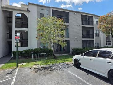 Gray condo building featuring outdoor parking, a bike rack, and a well-kept green lawn at 2030 Cascades Blvd # 204, Kissimmee, FL 34741