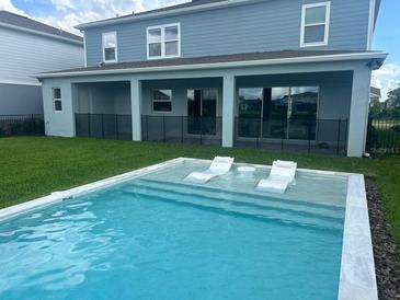 A backyard pool features built in lounge chairs, surrounded by a lush green lawn and the home's covered patio at 13467 Panama Beach Ct, Orlando, FL 32827