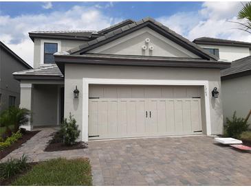 Beige two-car garage door in the front of a gray two-story home with a paved brick driveway and walkway at 1263 Verdant Glade Pl, Winter Park, FL 32792