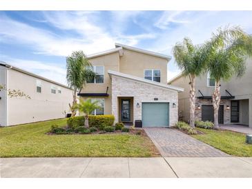 Two-story home with light beige walls and stone accents, a teal garage door, and landscaped yard at 601 Drop Shot Dr, Davenport, FL 33896