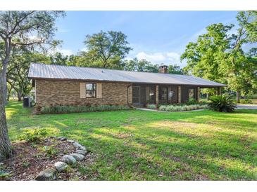 Brick ranch house with metal roof, landscaped yard, and screened porch at 1528 Walker Rd, Lakeland, FL 33810
