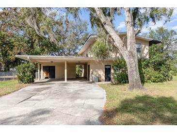 Beige two-story house featuring a covered carport, complemented by mature trees and manicured lawn at 819 22Nd Nw St, Winter Haven, FL 33881