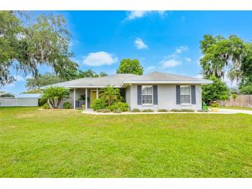 Charming single-story home featuring a well-manicured lawn, complemented by lush landscaping and a welcoming yellow front door at 1007 Cr 463B, Lake Panasoffkee, FL 33538