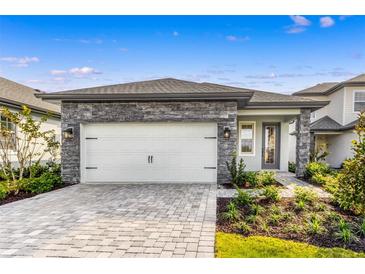 Charming home featuring a gray stone facade, a white garage door, and a brick paver driveway at 7701 Somersworth Dr, Kissimmee, FL 34747