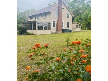 Charming two-story home featuring a screened porch, brick chimney, and blossoming orange flowers at 18700 Ravenswood Rd, Altoona, FL 32702
