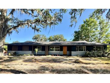 Charming single-story home with a modern exterior, painted in dark grey with an orange front door, under a shady tree at 3465 Peacock Ln, Mulberry, FL 33860