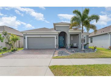 Charming single-story home features a well-manicured lawn, a brick driveway, and a cheerful blue front door at 140 Trinity Ridge Cir, Davenport, FL 33897