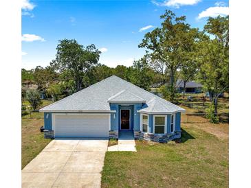 Charming home with a two-car garage, gray roof, and blue exterior paint under a partly cloudy sky at 12164 Se 85Th Ct, Belleview, FL 34420