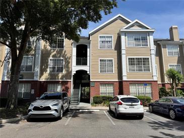 View of a tan and white two-story condo with red brick foundation and parked cars at 13103 Mulberry Park Dr # 833, Orlando, FL 32821