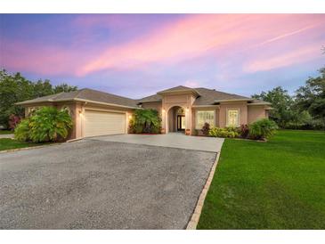 Beautiful single-story home features a two-car garage, archway entrance, and manicured landscaping with vibrant flowers and palm trees at 3979 Mammoth Grove Rd, Lake Wales, FL 33898