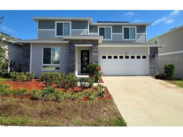Two-story home featuring a two-car garage, stone accents, and neatly landscaped front yard at 1123 Sugarwood St, Davenport, FL 33837