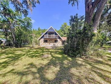 Charming two-story home with stone facade and balcony, surrounded by lush trees on a sunny day at 2900 Cr 415, Lake Panasoffkee, FL 33538
