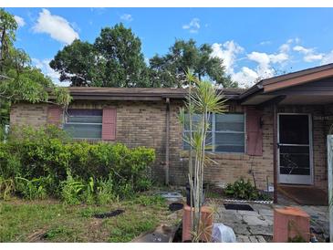Brick home exterior showing the front entrance and overgrown garden with a blue sky and white clouds at 115 Marjorie Ave, Auburndale, FL 33823