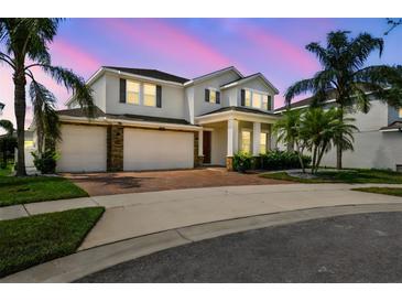 Elegant two-story home with a brick driveway, lush landscaping, and a three-car garage at twilight at 4950 Chase Ct, St Cloud, FL 34772