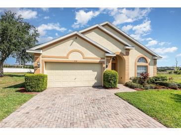 Charming single-story home with a brick driveway, two-car garage, and manicured landscaping under a bright sky at 908 Andalusia Loop, Davenport, FL 33837