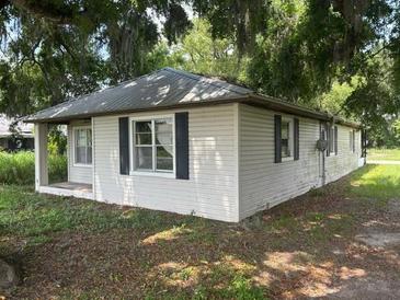 Cozy single story home with white siding and a metal roof surrounded by mature trees at 408 S Orange Ave, Fort Meade, FL 33841