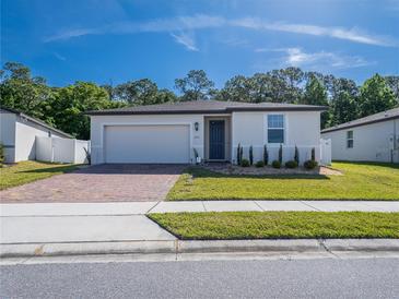 Charming single-story home features a well-manicured lawn, brick driveway, and a neutral-colored facade under a sunny sky at 573 Vista Villages Blvd, Davenport, FL 33896