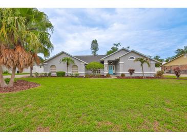 Well-maintained, light-gray home with a vibrant green lawn, palm trees, and a bright blue front door at 1034 Brighton Way, Lakeland, FL 33813