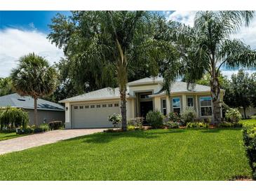 Well-maintained home featuring verdant lawn, mature palms, paver driveway, and attached garage at 10274 Julia Isles Ave, Oxford, FL 34484