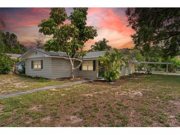 Charming single-story home features a mature tree, tidy landscaping, and a carport on a partly cloudy day at 107 Alachua Dr, Winter Haven, FL 33884