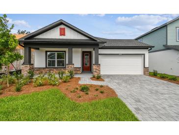 Charming single-story home with a well-manicured lawn, stone accents, gray driveway pavers and a two-car garage at 6068 Sacred Oak Ave, Mount Dora, FL 32757