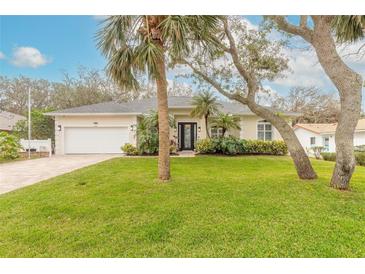 Tan house with white garage door, lush green lawn, and mature palm trees at 123 Ponce Terrace Cir, Ponce Inlet, FL 32127