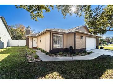 Tan house with white garage door, landscaped lawn, and walkway at 1413 La Paloma Cir, Winter Springs, FL 32708