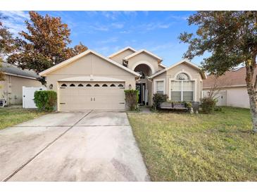 Tan house with a two-car garage and a well-maintained lawn at 3125 Wood Rose Way, Deltona, FL 32725