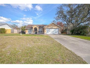 Tan single-story home featuring an attached two-car garage and a well-maintained front yard and long driveway at 893 S Dean Cir, Deltona, FL 32738