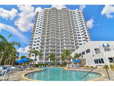 Luxury condominium building featuring a sparkling pool, palm trees, and blue umbrellas for relaxing by the water at 2 Oceans West Blvd # 1905, Daytona Beach Shores, FL 32118