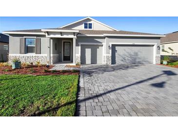 Charming single-story home featuring a stone facade, gray exterior, paver driveway, and well-manicured lawn at 875 Honey Petal Ln, Deland, FL 32720
