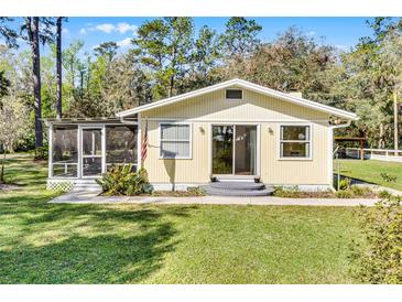 Charming single-story home with a screened porch, landscaped yard, and a cheerful, welcoming facade at 53722 Rivertrace Rd, Astor, FL 32102