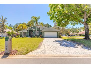 Charming green home with a well-manicured lawn, mature trees, and a brick-paved driveway leading to a two-car garage at 6 Greenvale Dr, Ormond Beach, FL 32174