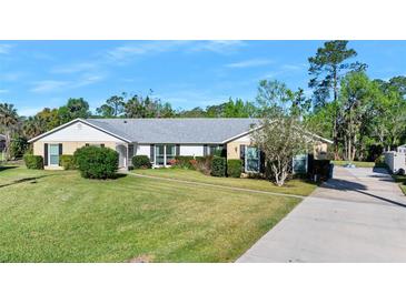 Charming single-story home with a well-manicured lawn, flowering bushes, and a long concrete driveway at 19 Twin River Dr, Ormond Beach, FL 32174