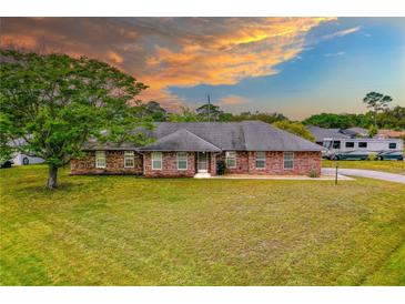 Charming single story brick home with a large lawn and mature tree, under a colorful sky at 3104 Umbrella Tree Dr, Edgewater, FL 32141