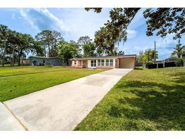 Ranch style home with pink siding, a concrete driveway, lush green lawn, and mature trees at 1160 Fountainhead Dr, Deltona, FL 32725