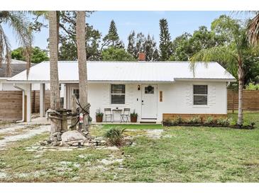 Charming white home with a metal roof, small outdoor seating, and lush landscaping at 104 Hester Ave, New Smyrna Beach, FL 32168