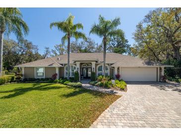 Charming home with a manicured lawn, brick driveway, and lush landscaping featuring palm trees at 6194 Half Moon Dr, Port Orange, FL 32127