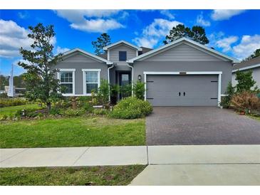 Charming single-Gathering home with gray siding, a well-manicured lawn, and a brick driveway at 1002 Chelan Falls Dr, Deland, FL 32724