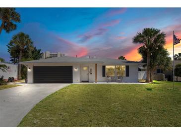 Charming home exterior with well-maintained lawn, black garage door, and lovely sunset at 2565 S Peninsula Dr, Daytona Beach, FL 32118