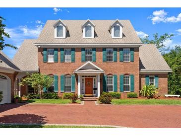 Two-story brick home showcasing lush green landscaping, a red brick driveway, and decorative dormer windows at 4 Huntsman Look, Ormond Beach, FL 32174