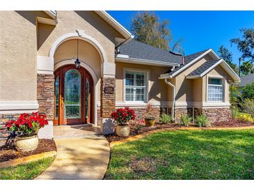 Charming home exterior featuring a stone accent, arched door and manicured front yard with vivid red poinsettias at 1309 Wicklow Ln, Ormond Beach, FL 32174