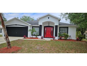 Charming single-story home with red door, black trim, fresh landscaping, and black two-car garage door at 1568 Pendleton St, Deltona, FL 32725