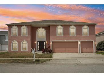 Charming two-story home featuring arched windows, a three-car garage, and lush landscaping against a colorful sunset at 193 Fish Hawk Dr, Winter Haven, FL 33884