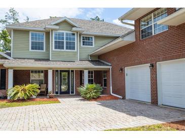 Two-story home with light green and brick exterior, manicured lawn, and two-car garage at 10 Foxhunter Flt, Ormond Beach, FL 32174