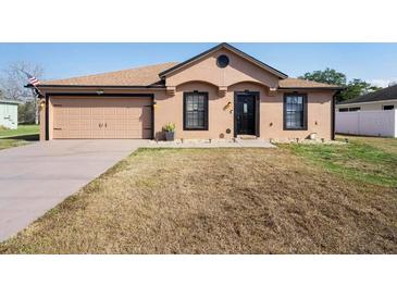 Tan single-story home with a two-car garage, brown roof, and tidy, drought-tolerant landscaping at 2448 Newmark Dr, Deltona, FL 32738